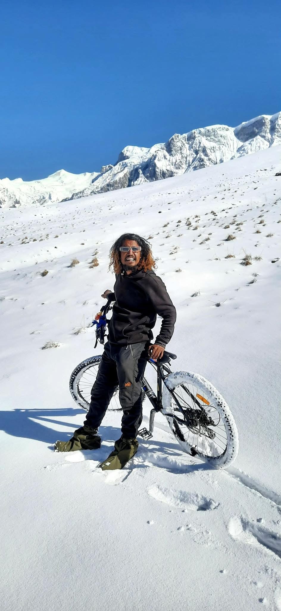Ajit with bike in deep snow, Himalayan peaks behind