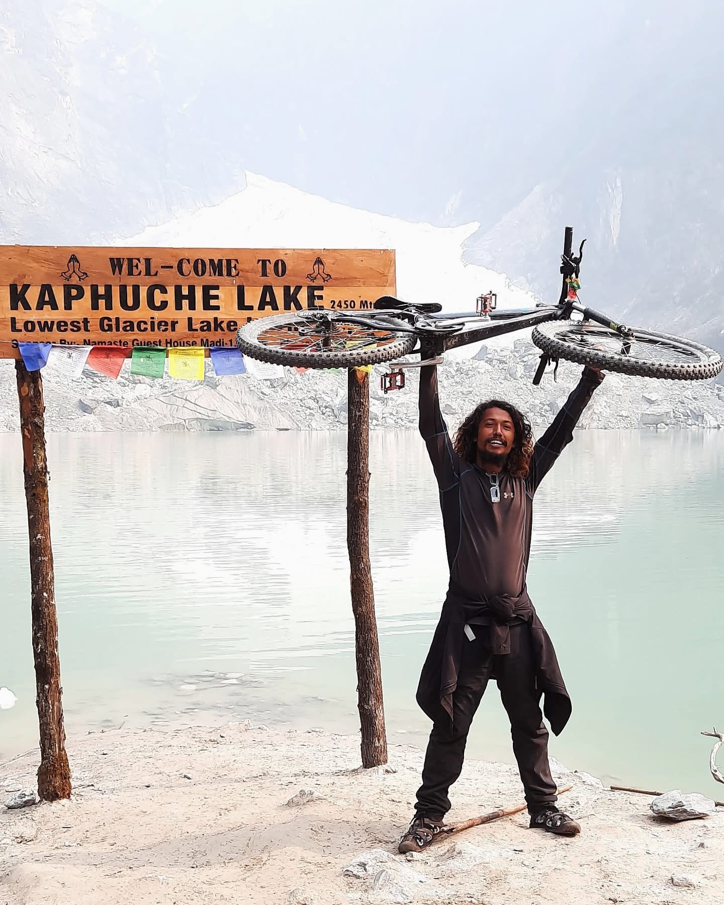 Raising bike overhead at Kaphuche Lake glacier sign