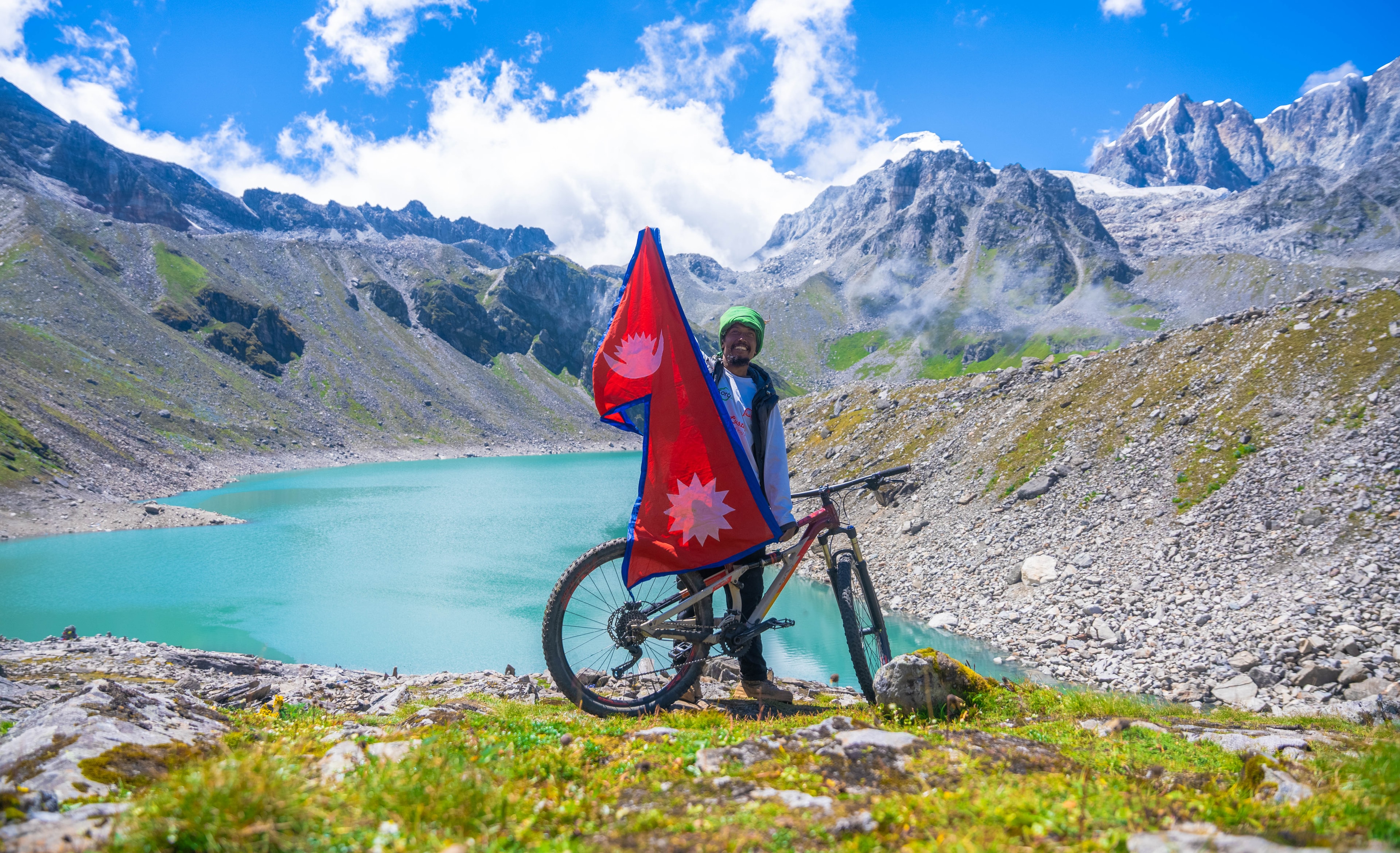 Cyclist holding Nepal flag at mountain lake